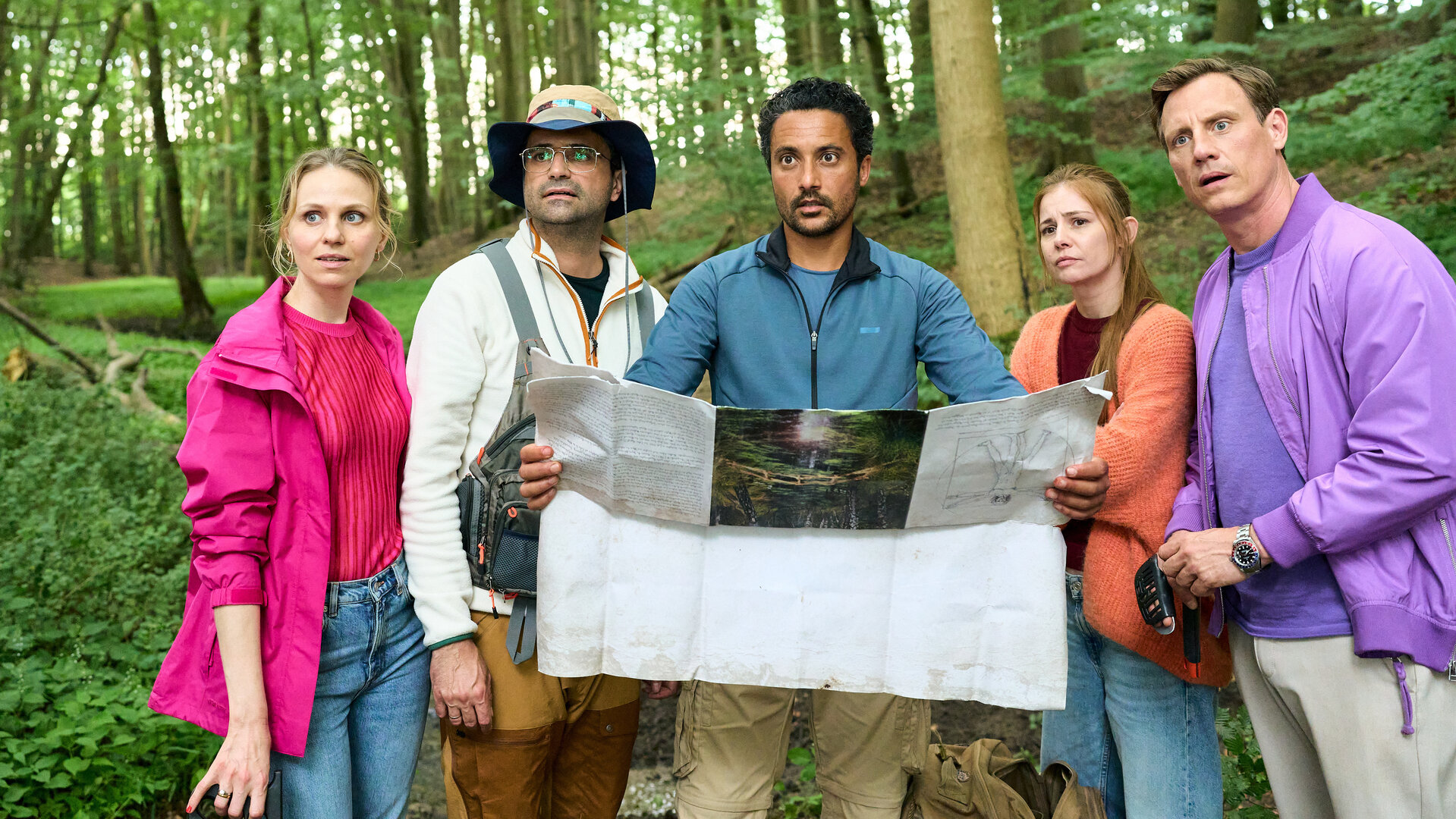 "Dr. Nice - Die Natur der Liebe": Naturpädagoge Deniz Birol (Omar El-Saeidi) hält eine Landkarte vor sich und erklärt den verwundert schauenden Teilnehmenden an seiner Exkursion in die Natur, was für Aufgaben sie zu lösen haben. Nice (Patrick Kalupa) sieht nicht begeistert aus, Charlie (Josefine Preuß) steht neben ihm und schaut skeptisch, während Dr. Schmidtke (Maximilian Grill) und seine Frau Jana (Tereza Rizos) aussehen, als ob sie sich auf den Ausflug freuen.