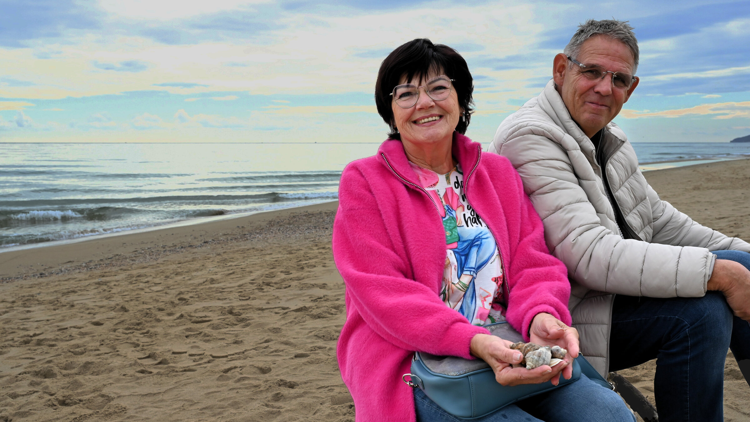 "ZDF.reportage: Rentnerglück Bulgarien - Leben für die Hälfte": Marlene und Jürgen sitzen am Strand. Beide schauen lächelnd in die Kamera.