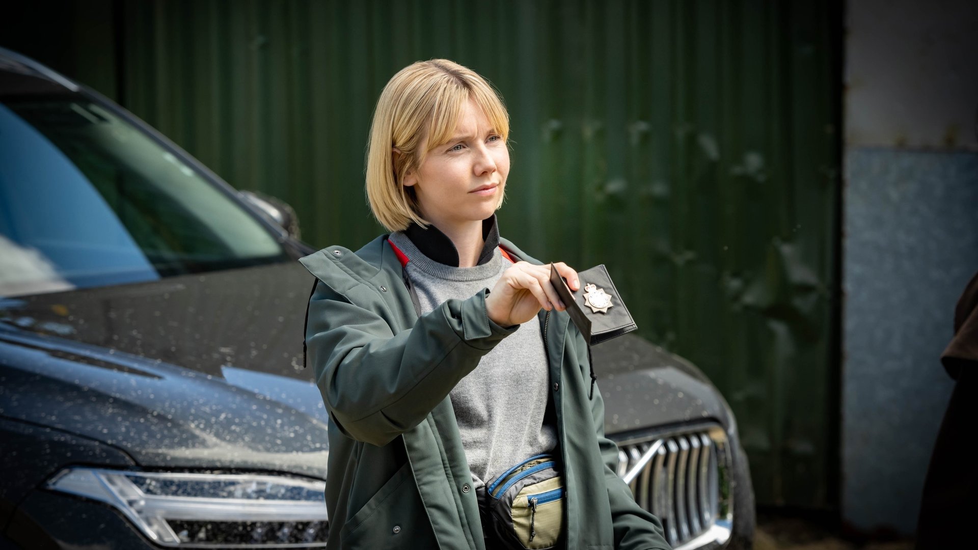 "Karen Pirie - Echo einer Mordnacht - Der Fall Rosie Duff": DS Karen Pirie (Lauren Lyle) steht vor einem großen SUV und zeigt ihrem Gegenüber (nicht im Bild) ihre Polizeimarke.