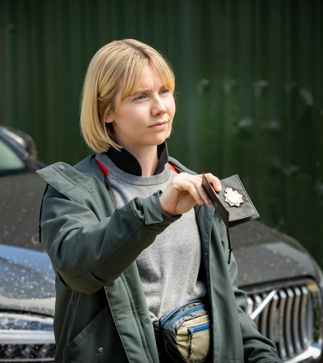 "Karen Pirie - Echo einer Mordnacht - Der Fall Rosie Duff": DS Karen Pirie (Lauren Lyle) steht vor einem großen SUV und zeigt ihrem Gegenüber (nicht im Bild) ihre Polizeimarke.