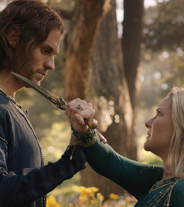 "Der Herr der Ringe: Die Ringe der Macht - Gebunden": Galadriel (Morfydd Clark) und Halbrand (Charlie Vickers) stehen sich in einem Wald gegenüber. Sie hält einen Dolch in seine Richtung. Er wehrt ihre Bewegung ab.
