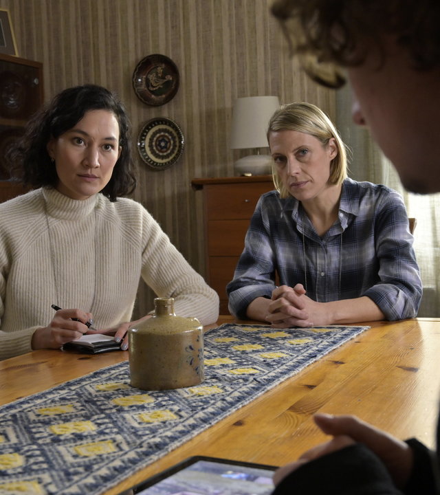 "SOKO Potsdam - Fremder Vertrauter": An einem Esszimmertisch aus Holz sitzen die beiden  Kommissarinnen Pauline Hobrecht (Agnes Decker) und Tamara Meurer (Anja Pahl). Gegenüber von ihnen, mit dem Rücken zur Kamera, sitzt Tim Demandt (Jean Luc Caputo). Mit ernsten Blicken, sehen sie Tim Demandt an. In der rechten Hand hält Pauline Hobrecht einen Stift, vor ihr auf dem Tisch liegt ein Notizblock. Tim Demandt hat ein Tablet vor sich auf dem Tisch liegen.