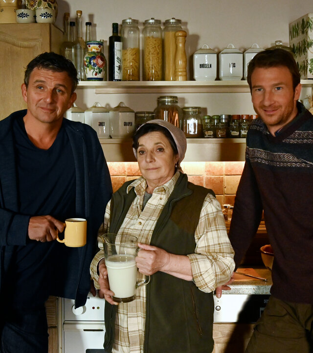 "Der Bergdoktor: Die dunkle Seite des Lichts": Martin (Hans Sigl), Lisbeth (Monika Baumgartner) und Hans (Heiko Ruprecht) stehen zusammen vor einer Küchenzeile und schauen in die Ferne.