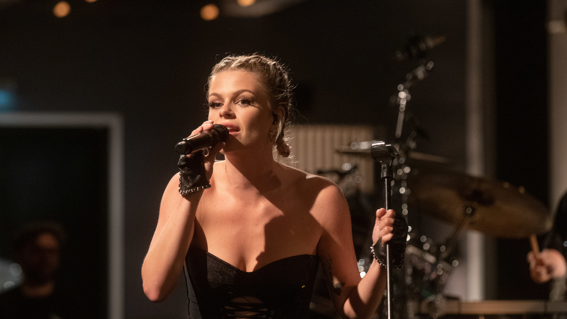 "Pop Around @ Bauhaus: Davina Michelle": Eine junge blonde Frau mit geflochtenen Zöpfen steht auf der Bühne und singt in ein Mikro. Sie trägt schwarze Kleidung, im Hintergrund sind Musiker zu sehen.