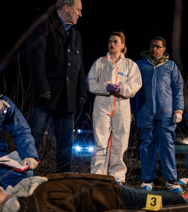 "SOKO München - Fünf Minuten": Am Tatort - Es ist dunkel. Im Hintergrund sind Scheinwerfer eines Polizeiautos zu sehen. Neben einer Gleise liegt eine Leiche auf dem Boden, Dr. Weissenböck (Florian Odendahl) sitzt in der Hocke daneben und ermittelt, er hat eine kleine Taschenlampe in der Hand. Neben ihm stehen Arthur Bauer (Gerd Silberbauer), Billie Curio (Sina Reiß), Franz Ainfachnur (Christofer v. Beau) und Dominik Morgenstern (Joscha Kiefer) und besprechen sich.