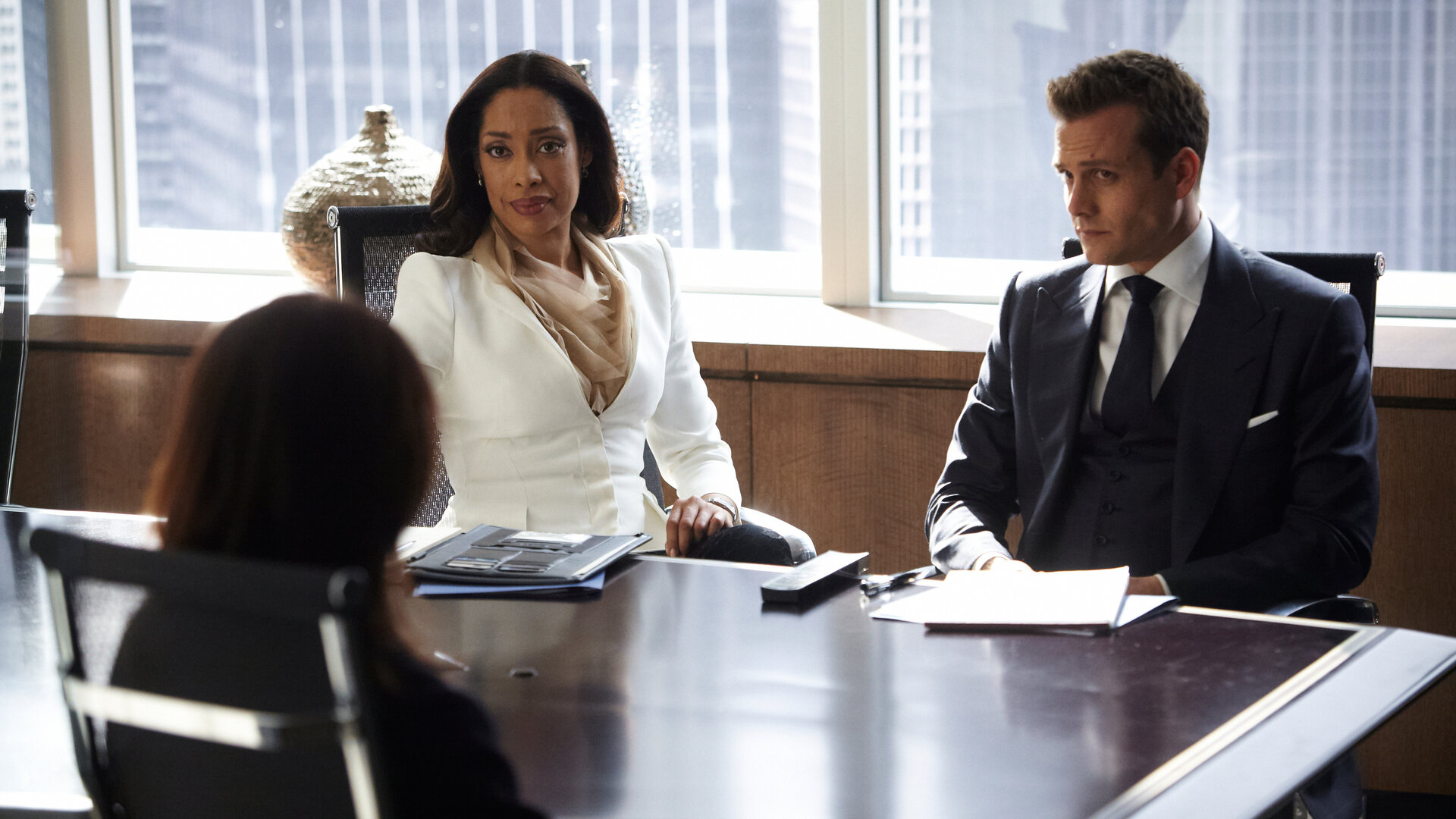 "Suits - Partnerwahl": Jessica (Gina Torres) und Harvey (Gabriel Macht) sitzen nebeneinander an einem Konferenztisch und blicken zu Ava Hessington (Michelle Fairley), die ihnen gegenüber Platz genommen hat. Auf dem Tisch zwischen ihnen liegen Akten und Notizen.