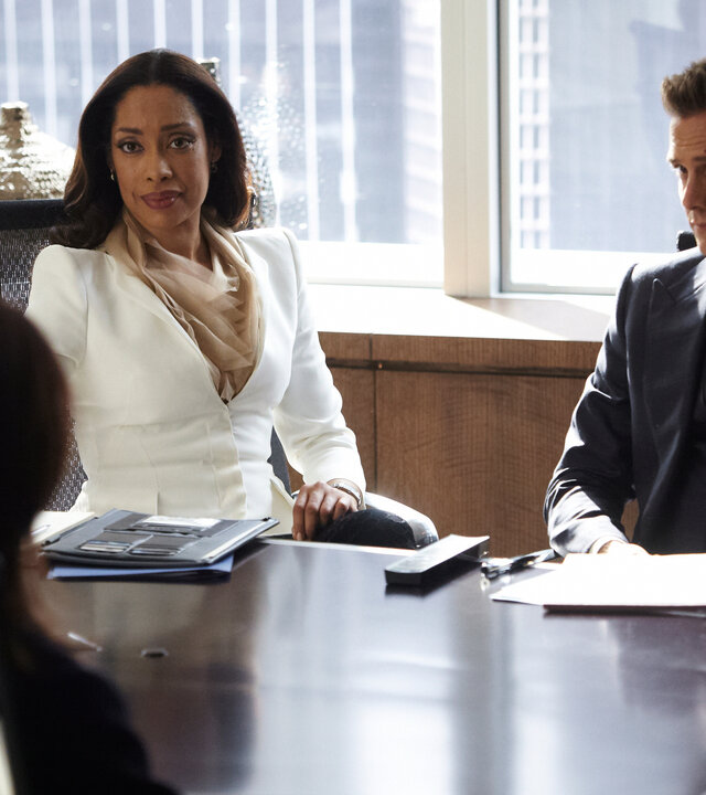 "Suits - Partnerwahl": Jessica (Gina Torres) und Harvey (Gabriel Macht) sitzen nebeneinander an einem Konferenztisch und blicken zu Ava Hessington (Michelle Fairley), die ihnen gegenüber Platz genommen hat. Auf dem Tisch zwischen ihnen liegen Akten und Notizen.