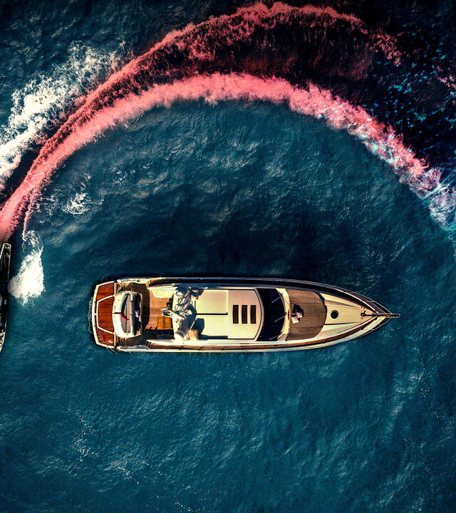 "Die Yacht": Luftaufnahme: Eine kleine, cremefarbene Yacht wird auf offener See von einem  schwarzen Motorboot umkreist. Die Spur des Motorbootes im Wasser ist rot eingefärbt, um eine Blutspur zu suggerieren.