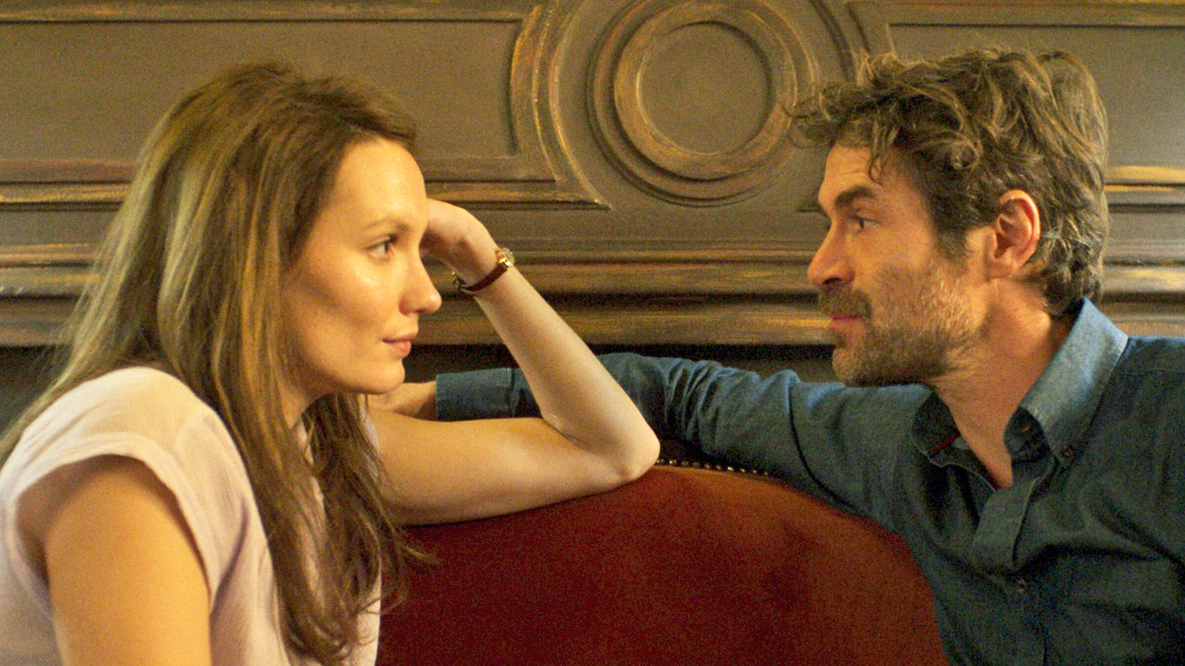 "La Maison – Haus der Lust": Emma (Ana Girardot) und Stéphane (Yannick Renier) sitzen sich auf einem Sofa gegenüber und schauen sich an.
