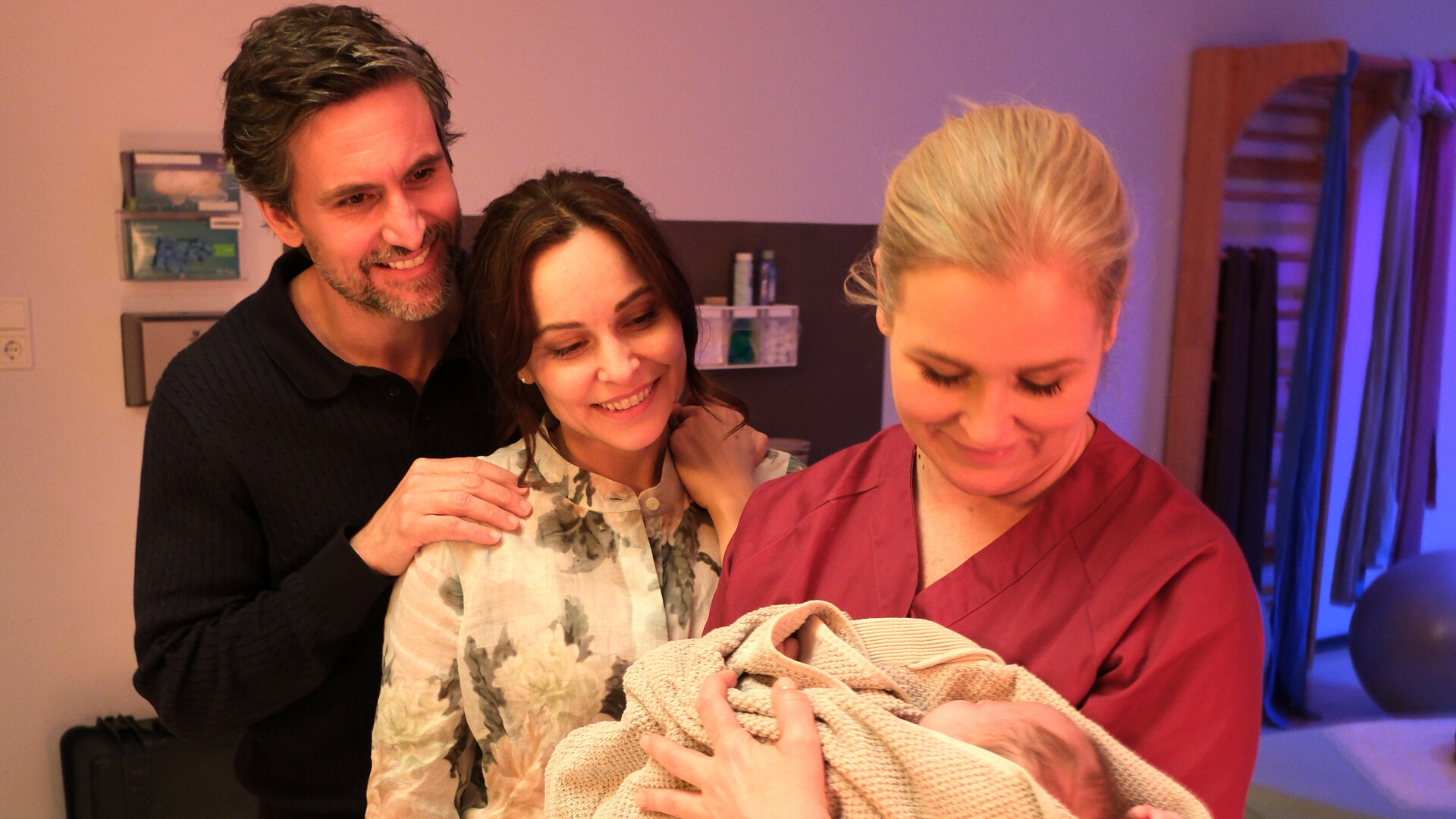 "Lena Lorenz - Muttergefühle": In einem Kreißsaal hält Lena Lorenz (Judith Hoersch) ein Baby im Arm, das in eine Decke gewickelt ist und betrachtet es lächelnd. Jan (Tom Beck) und Katina Wolff (Mina Tander) stehen mit strahlendem Lächeln daneben und schauen das Baby freudig an.