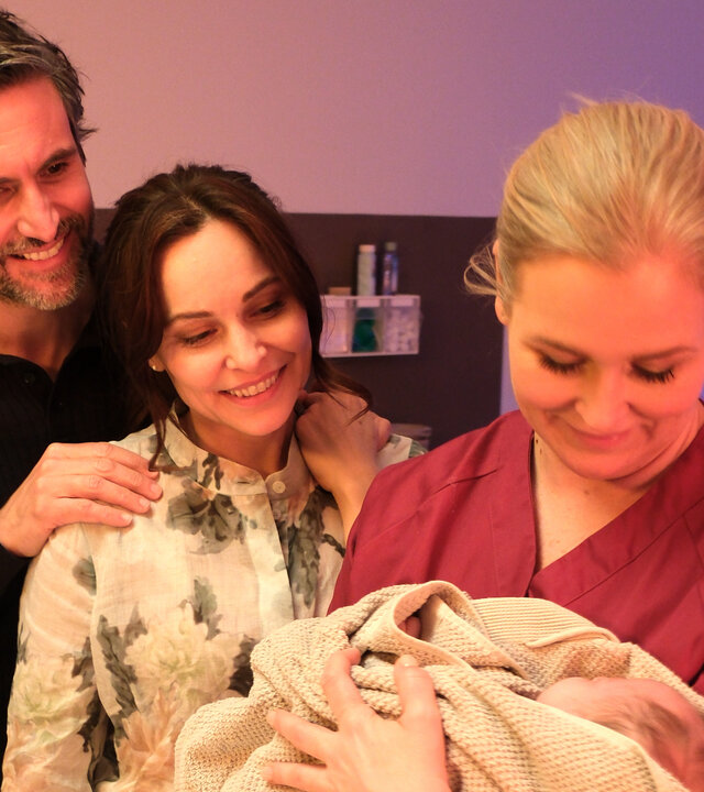 "Lena Lorenz - Muttergefühle": In einem Kreißsaal hält Lena Lorenz (Judith Hoersch) ein Baby im Arm, das in eine Decke gewickelt ist und betrachtet es lächelnd. Jan (Tom Beck) und Katina Wolff (Mina Tander) stehen mit strahlendem Lächeln daneben und schauen das Baby freudig an.