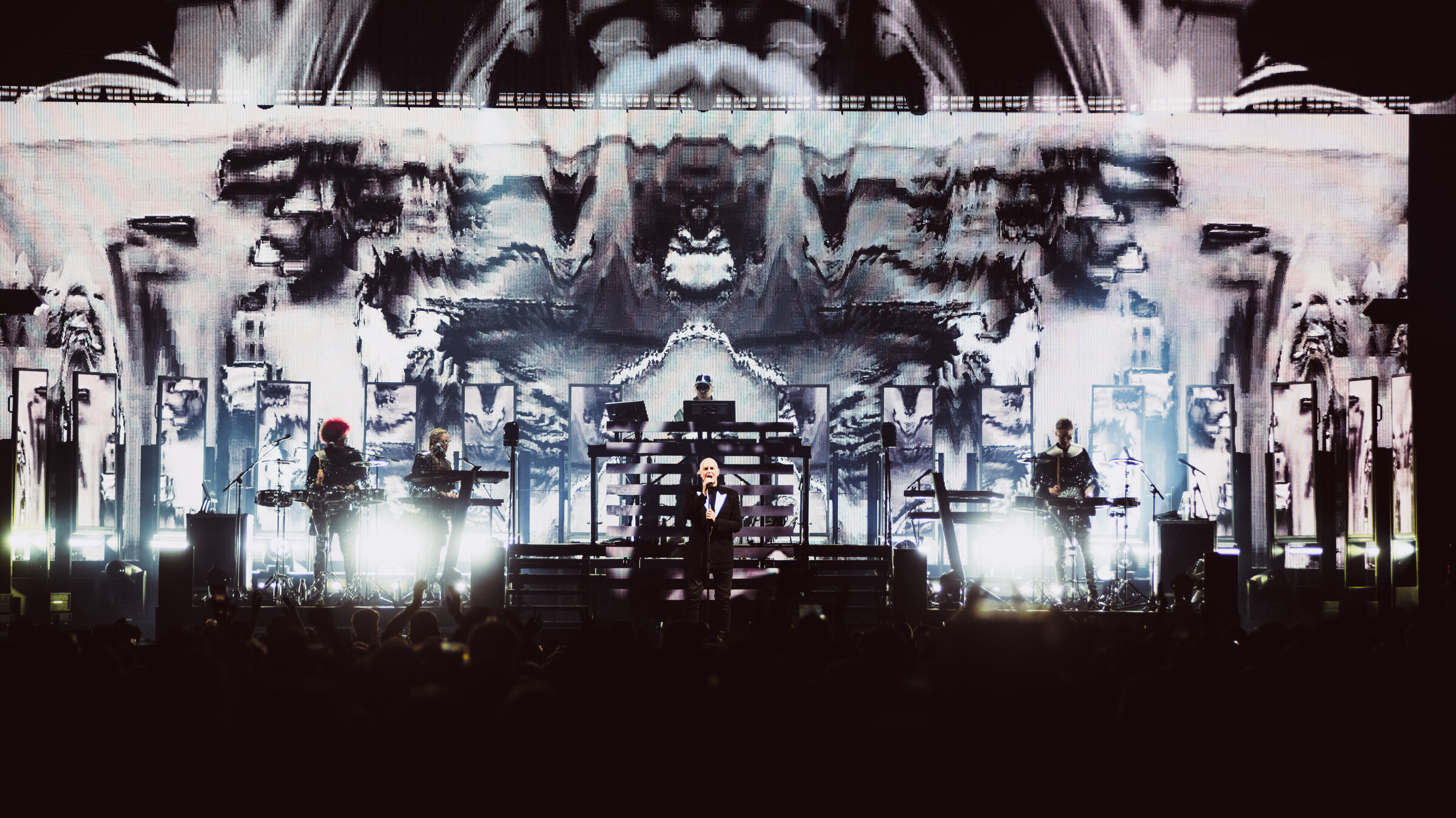 "Pet Shop Boys: Dreamworld": Das Duo Pet Shop Boys begleitet von einer Band während eines Konzerts auf einer Bühne. Mittig steht der Sänger mit einem Mikrofon in der Hand. Im Hintergrund ein aufwändiges Bühnenbild mit Projektionen und Lichteffekten.