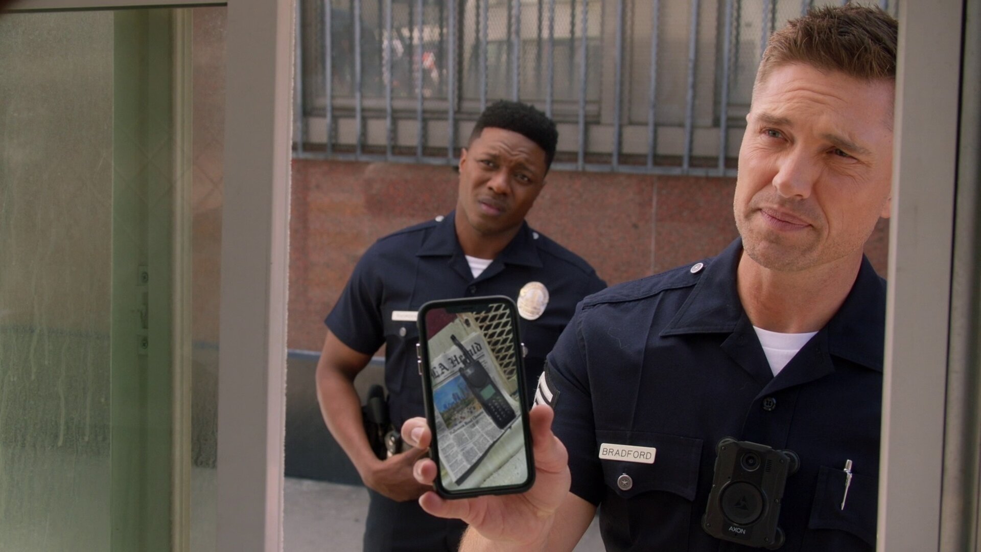 "The Rookie - Alte Wunden": Officer Tim Bradford (Eric Winter) zeigt seinem Gegenüber ein Foto des Polizeifunkgeräts auf seinem Smartphone, während Aaron Thorsen (Tru Valentino) skeptisch zuschaut.