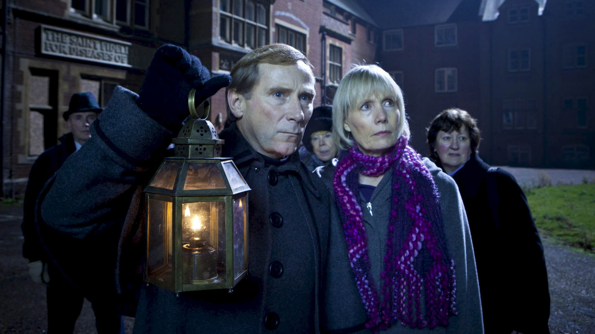 "Inspector Barnaby - Geisterwanderung": Jeff Bowmaker (Danny Webb) und Joyce Barnaby (Jane Wymark) stehen im Dunkeln vor einem Haus. Hinter ihnen stehen weitere Personen.