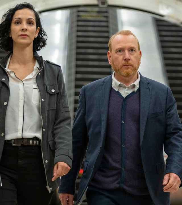 "The Chelsea Detective - Der Preis der Sünde": Priya Shamsie (Sonita Henry) und Max Arnold (Adrian Scarborough) sind am Bahnsteig der U-Bahn Station angekommen. Im Hintergrund die Rolltreppen der U-Bahn Station.