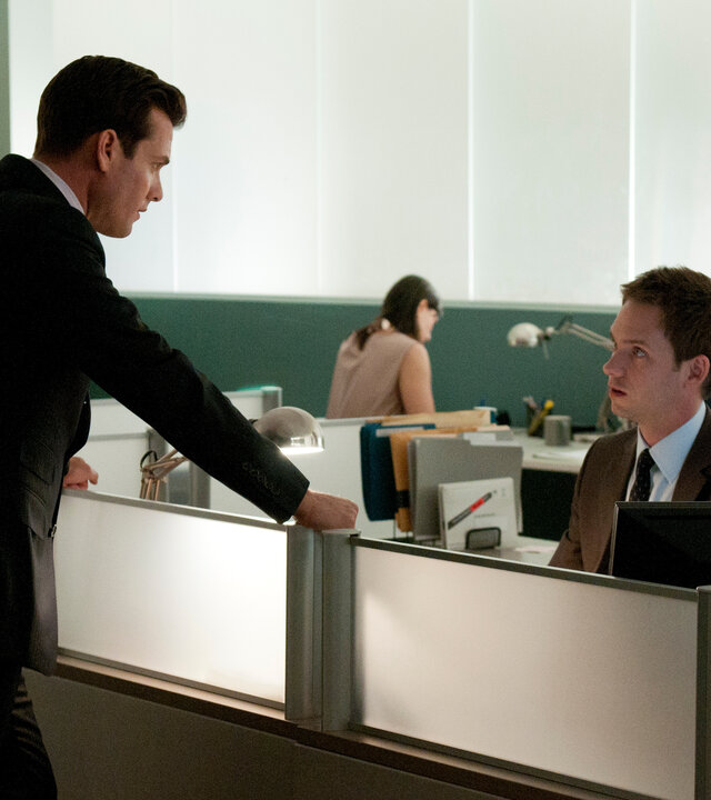 "Suits - Moralische Bedenken": Harvey (Gabriel Macht) steht an Mikes (Patrick J. Adams) Arbeitsplatz und stützt sich mit beiden Händen auf die Trennwand. Mike sitzt im Anzug vor seinem Computer und blickt ihn ernst an. Im Hintergrund arbeiten weitere Personen an ihren Schreibtischen.