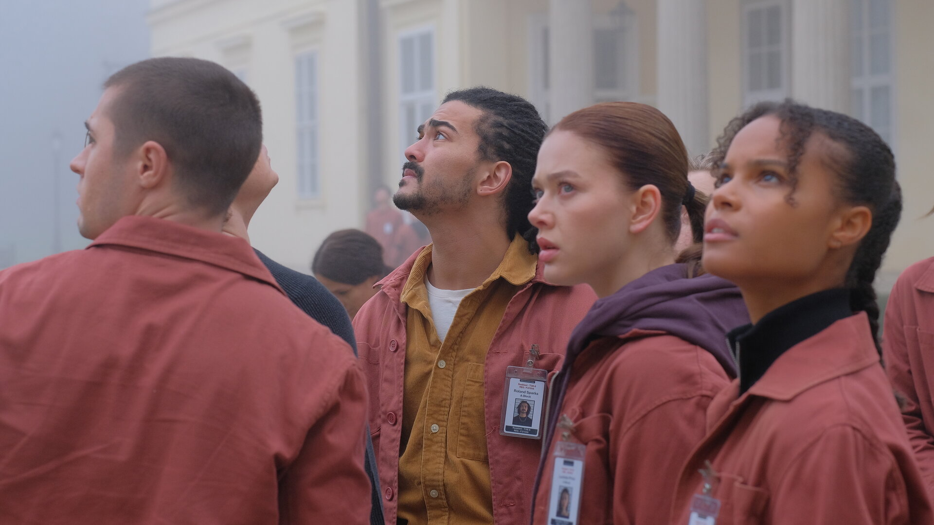 "Fallen - Schatten": Daniel (Gijs Blom), Roland (Lawrence Walker), Luce (Jessica Alexander) und Gabbe (Indeyarna Donaldson-Holness) blicken angespannt nach oben. Im Hintergrund ist ein helles Gebäude im dichten Nebel zu erkennen.