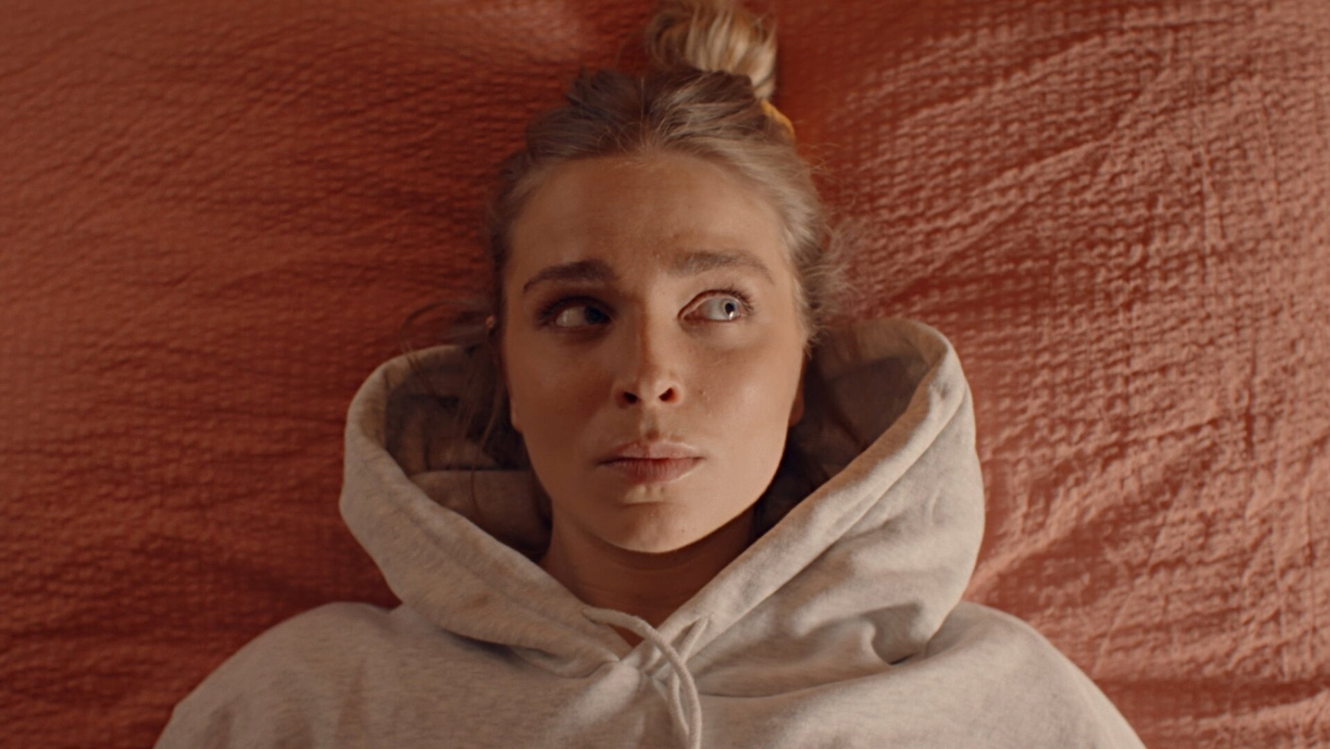 "Single Bells - 12 Dates till Christmas: Jens II": Blick von oben: Mina (Julie Van den Steen) liegt mit einem hellgrauen Hoodie bekleidet auf einem Kissen mit orangefarbenem Bezug.