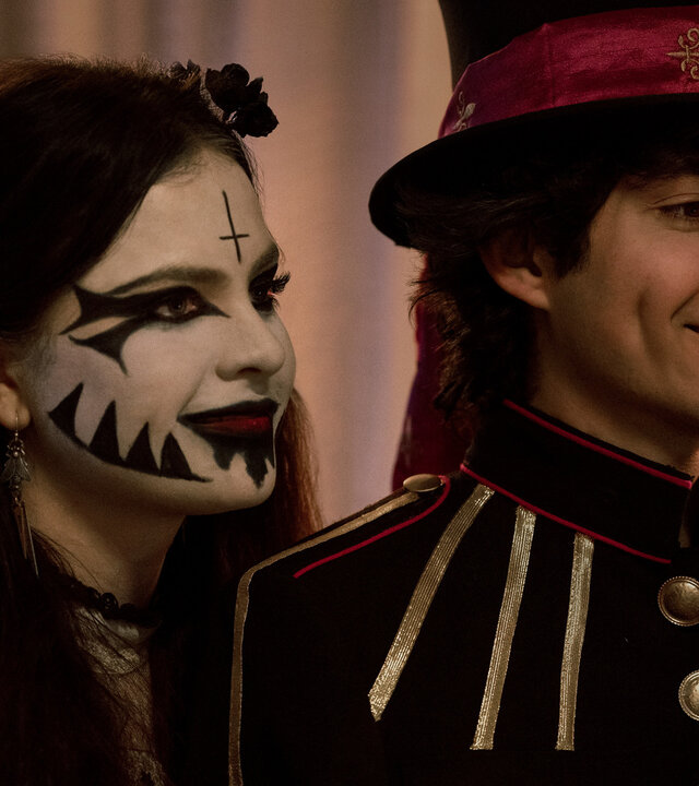 "Hysteria! - Die Ankunft des Bösen": Jordy (Chiara Aurelia) und Dylan (Emjay Anthony) stehen nebeneinander und blicken lächelnd in dieselbe Richtung. Jordy trägt ein auffälliges Make-up mit schwarzem Muster und ein dunkles Outfit, während Dylan eine Uniformjacke mit Zierknöpfen und einen Zylinder mit rotem Band trägt.