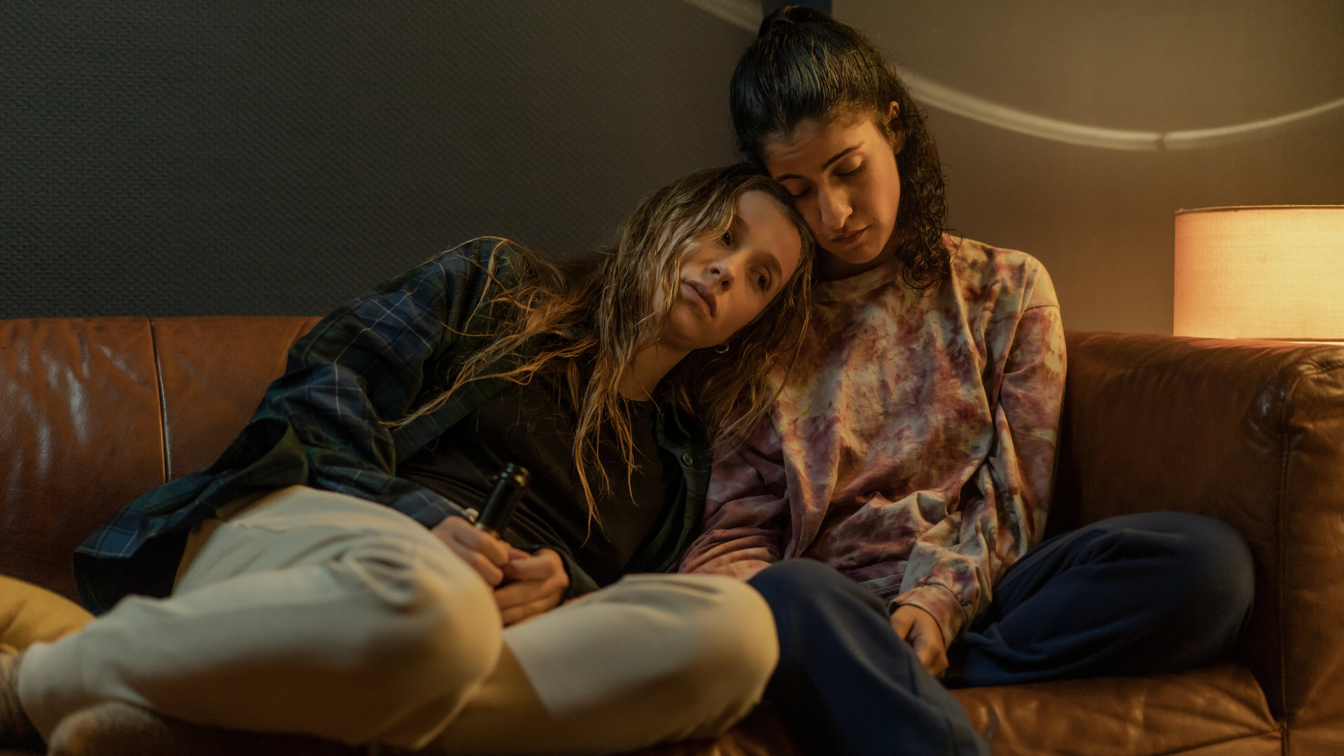 "Loving Her - Loving Lies": Hanna (Banafshe Hourmazdi) und Franzi (Lena Klenke) sitzen nebeneinander auf dem Sofa. Franzi hat sich an Hanna gelehnt. Ihr Kopf liegt auf ihrer Schulter.