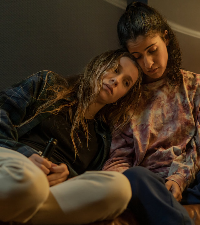 "Loving Her - Loving Lies": Hanna (Banafshe Hourmazdi) und Franzi (Lena Klenke) sitzen nebeneinander auf dem Sofa. Franzi hat sich an Hanna gelehnt. Ihr Kopf liegt auf ihrer Schulter.