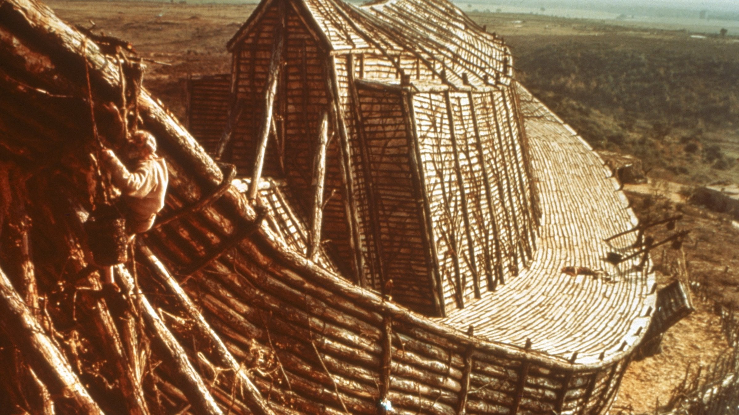 "Die Bibel": Zu sehen ist ein riesiges Schiff aus Holz mit großem Aufbau in der Mitte. Vorne links klettert Noah in luftiger Höhe, um letzte Arbeiten zu erledigen. Im Hintergrund ist eine weite, karge Landschaft zu sehen.