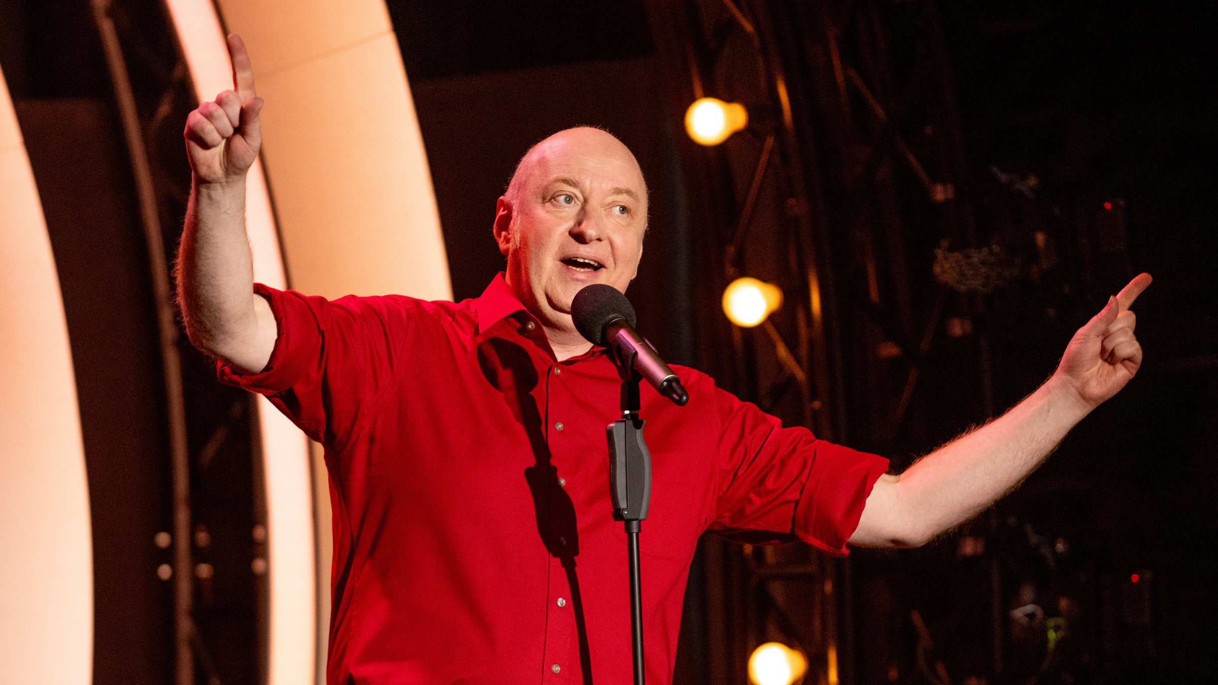 "Horst Evers: Wer alles weiß, hat keine Ahnung": Horst Evers steht auf der Bühne und präsentiert sein neues Programm. Er trägt ein rotes Hemd und eine schwarze Hose.