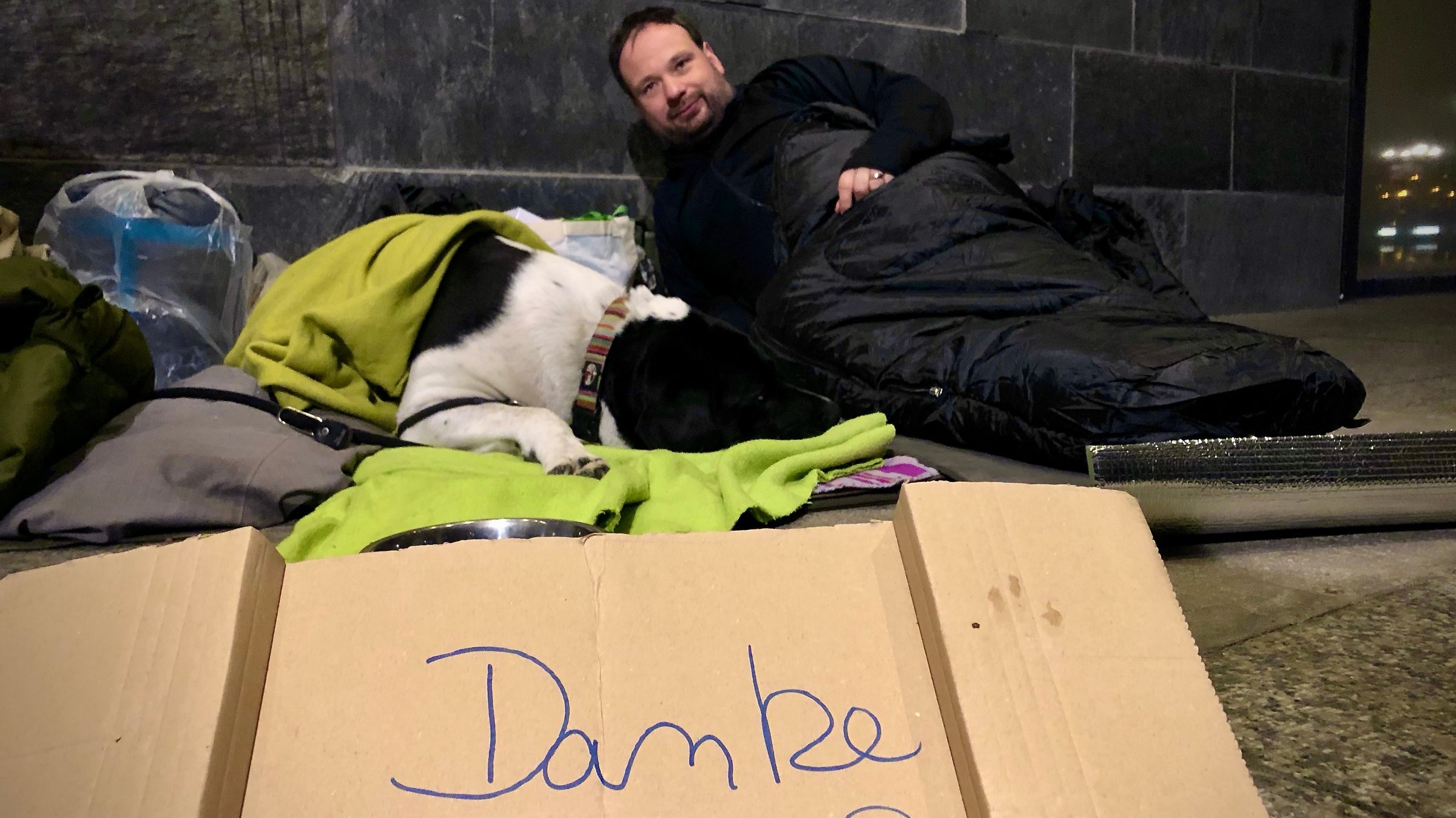 "Ein guter Grund zu feiern - Dreikönig mit Pater Nikodemus Schnabel": Pater Nikodemus liegt zu Fuße des Kölner Doms mit einem Schlafsack. Vor ihm ein Pappschild mit der Aufschrift "Danke".