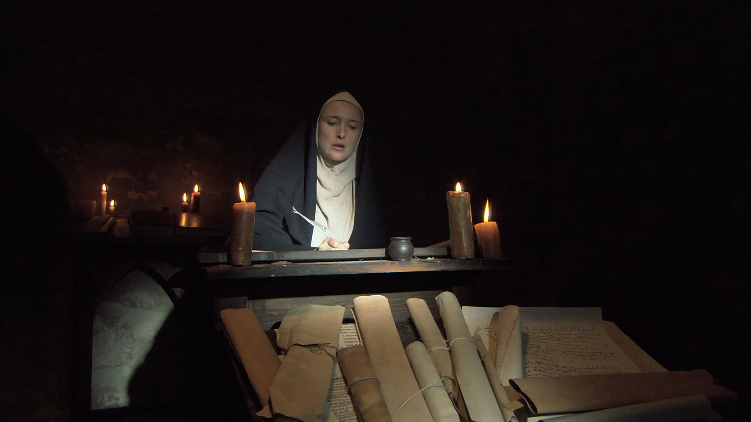 "Die glorreichen 10 - Die erfolgreichsten Mediziner der Geschichte": Darstellerin der Hildegard von Bingen sitzt in einem mit Kerzen beleuchteten Klosterraum an einem Pult und schreibt.