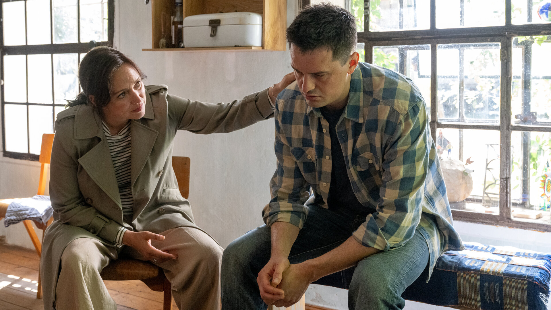 "SOKO Wismar – Die Kirchenmalerin": In der Wohnküche des Opfers sitzt Kriminalhauptkommissarin Karoline Joost (Nike Fuhrmann) neben Max Artner (Jannik Mioducki), dem Lebensgefährten der Toten. Sie legt ihm tröstend die Hand auf die Schulter.