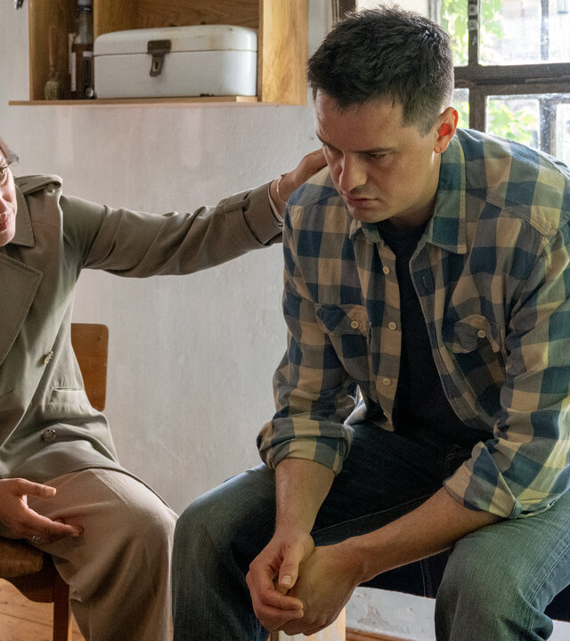 "SOKO Wismar – Die Kirchenmalerin": In der Wohnküche des Opfers sitzt Kriminalhauptkommissarin Karoline Joost (Nike Fuhrmann) neben Max Artner (Jannik Mioducki), dem Lebensgefährten der Toten. Sie legt ihm tröstend die Hand auf die Schulter.