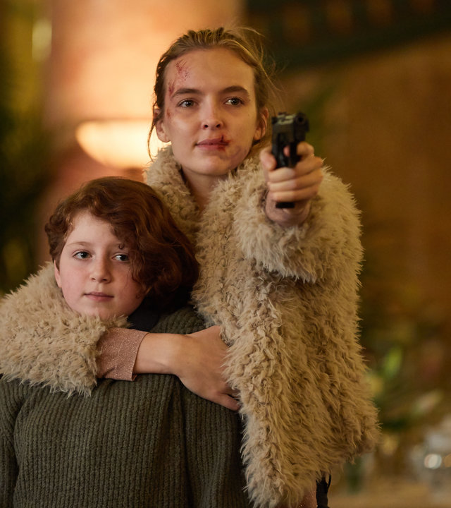 "Killing Eve - Gott, bin ich müde": Villanelle (Jodie Comer) hält Irina (Yuli Lagodinsky) in einem schicken Restaurant nah bei sich und zielt gleichzeitig mit einer Pistole nach vorne.