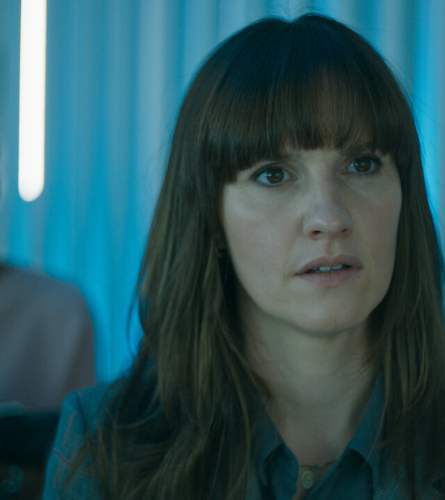 "Concordia - Tödliche Utopie (2) - Der Verdacht": Thea Ryan (Ruth Bradley) steht in einem Innenraum und schaut zur Seite. Hinter ihr steht, unscharf zu erkennen, Isabelle Larsson (Nanna Blondell).