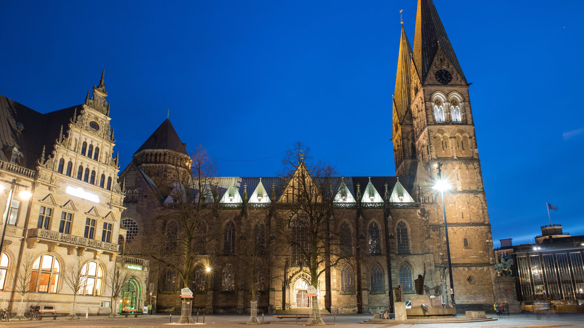 "Ökumenischer Gottesdienst zum Tag der Deutschen Einheit: Viel Stärken - Ein Land": Der beleuchtete Bremer St. Petri-Dom hebt sich vom blauen Abendhimmel ab. Neben dem Dom befindet sich das historische Bremer Rathaus.