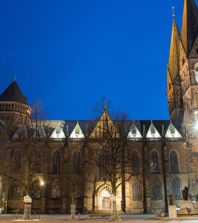 "Ökumenischer Gottesdienst zum Tag der Deutschen Einheit: Viel Stärken - Ein Land": Der beleuchtete Bremer St. Petri-Dom hebt sich vom blauen Abendhimmel ab. Neben dem Dom befindet sich das historische Bremer Rathaus.