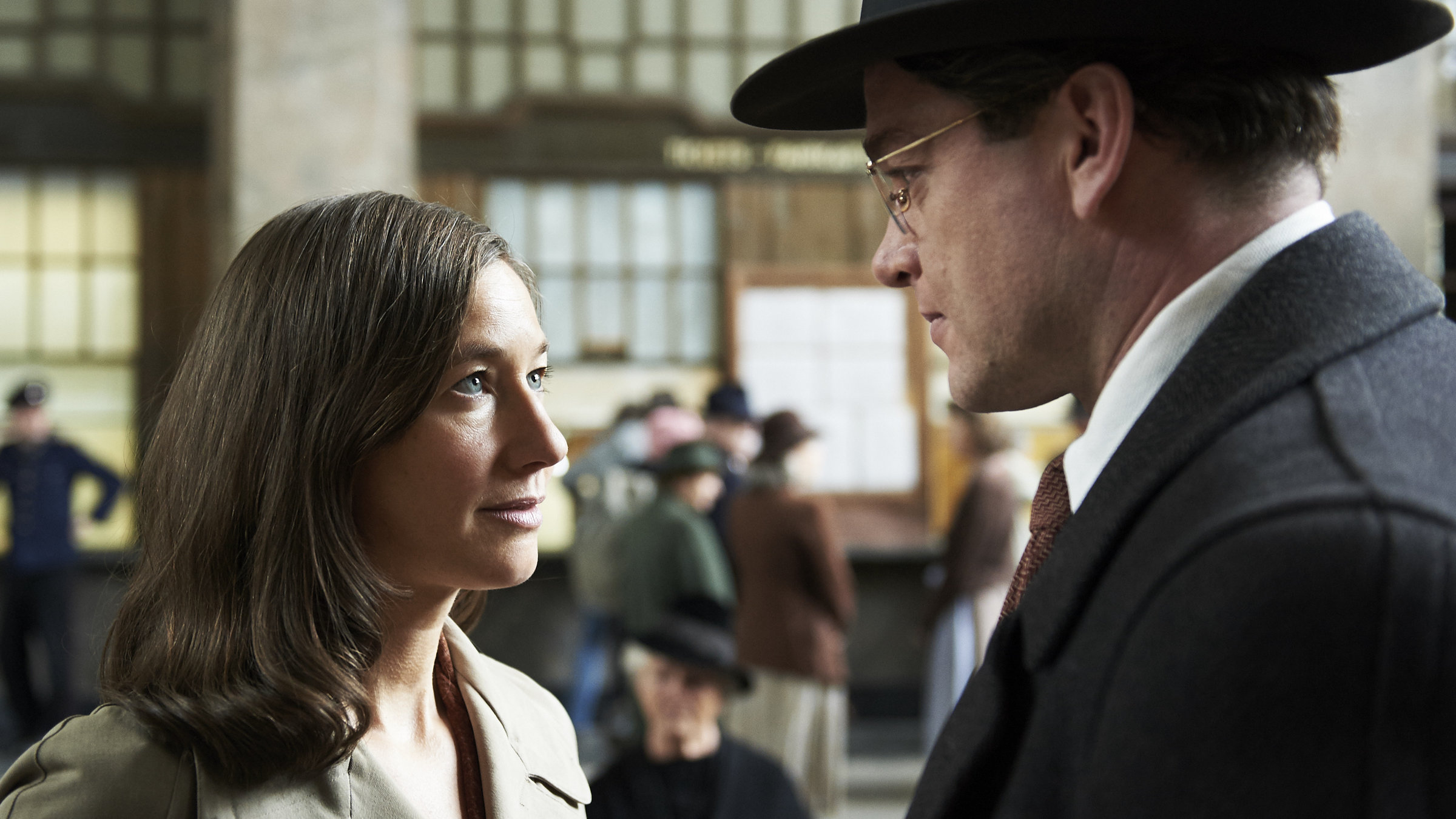 "Landgericht - Geschichte einer Familie (2)": Richard (Ronald Zehrfeld) und Claire (Johanna Wokalek) stehen in einer Bahnhofshalle und schauen einander an.