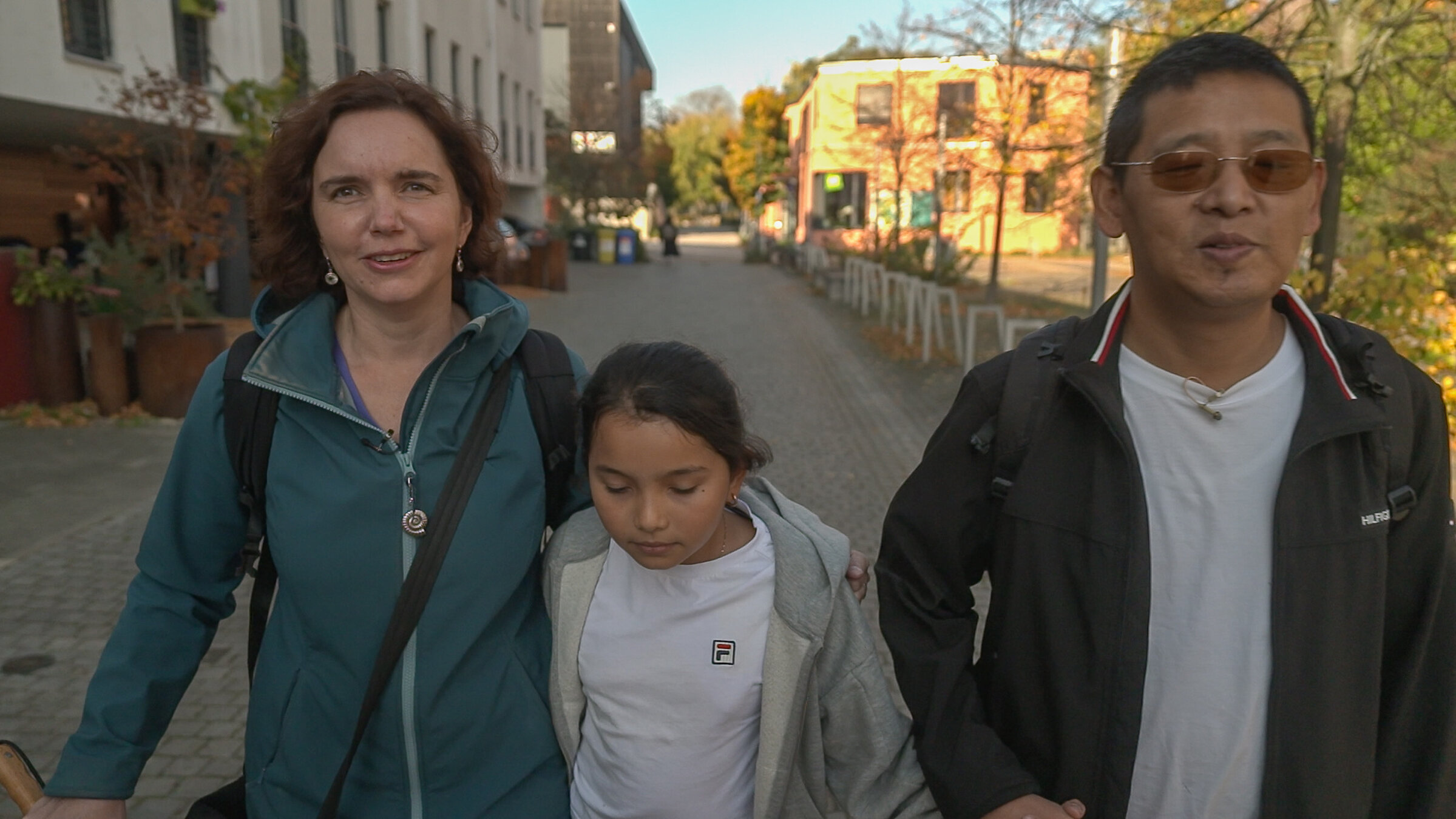 "Einfach Mensch - Familie mit Behinderung": Gendun, Mila und Hannah laufen nebeneinander auf einem Bürgersteig auf die Kamera zu.