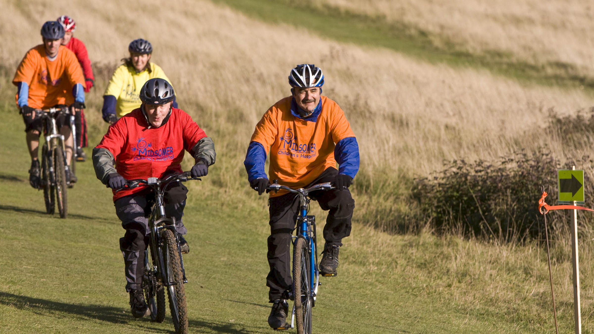 "Inspector Barnaby - Sag Ja und stirb!": George Jeffers (David Haig) und Edward Canning (Jim Norton) fahren nebeneinander Fahrrad auf einem Feldweg. Hinter ihnen sind weitere Wettkampfteilnehmer.