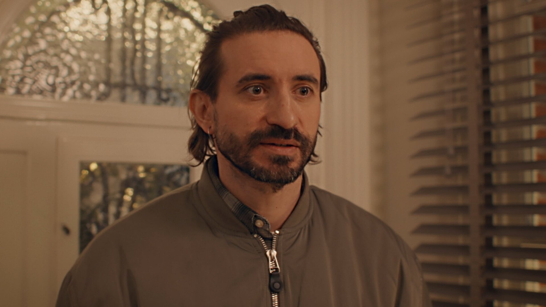 "Single Bells - 12 Dates till Christmas: Pascal": Pascal (Bill Barbedis) steht im Flur vor der Haustür. Er hat einen gestutzten Vollbart und trägt eine sportliche, hochgeschlossene Jacke. Er schaut erwartungsvoll.