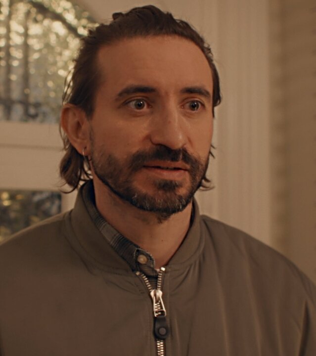 "Single Bells - 12 Dates till Christmas: Pascal": Pascal (Bill Barbedis) steht im Flur vor der Haustür. Er hat einen gestutzten Vollbart und trägt eine sportliche, hochgeschlossene Jacke. Er schaut erwartungsvoll.