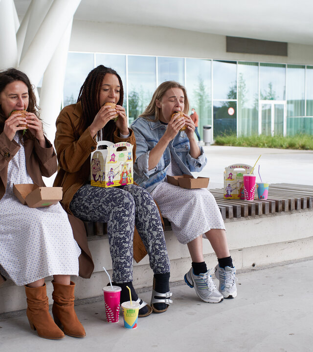 "The Club - Der Geburtstagskarten-Club": Kirstie (Janne Desmet), Ellen (Jade Olieberg) und Charlie (Roos Dickmann) essen genüsslich Burger vor der Klinik.