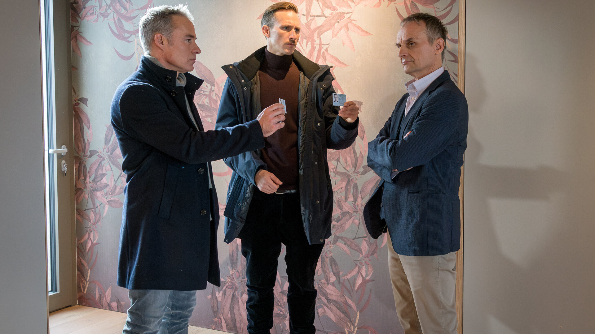 "SOKO Leipzig - Mein Vater, dein Vater": In einem Innenraum: Jan Maybach (Marco Girnth) und Moritz Brenner (Johannes Hendrik Langer) halten Peter Gundermann (Ingolf Müller-Beck) ihre Dienstausweise hin, der jedoch unbeeindruckt und mit verschränkten Armen stehen bleibt.