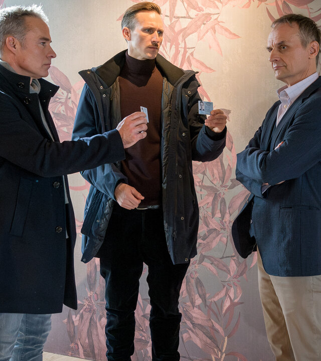 "SOKO Leipzig - Mein Vater, dein Vater": In einem Innenraum: Jan Maybach (Marco Girnth) und Moritz Brenner (Johannes Hendrik Langer) halten Peter Gundermann (Ingolf Müller-Beck) ihre Dienstausweise hin, der jedoch unbeeindruckt und mit verschränkten Armen stehen bleibt.