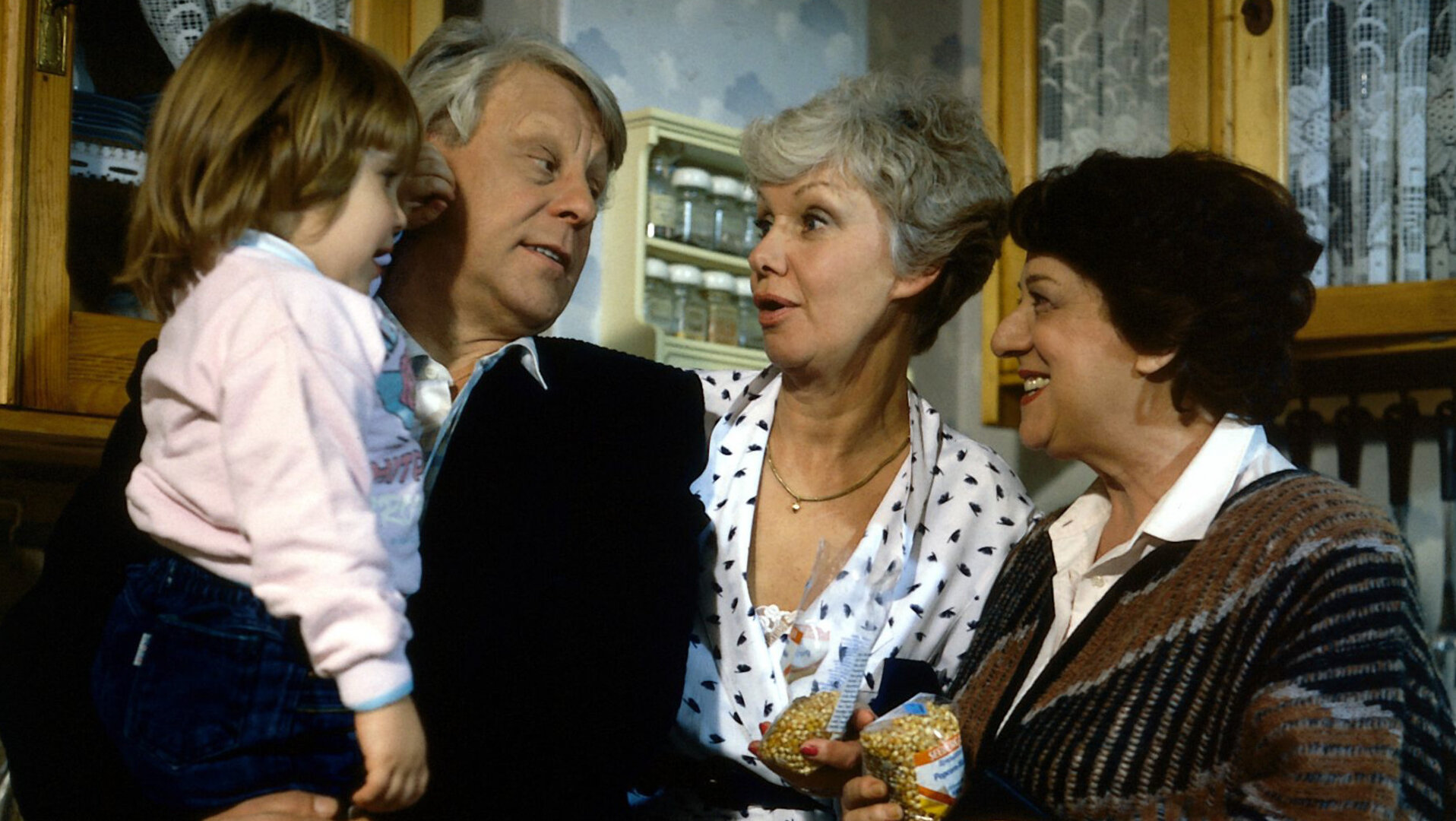 "Die Wicherts von nebenan: Der Prinz von Arkadien": Gerda (Inge Wolffberg) hat eine Tüte Mais für Popcorn in der Hand. Eberhard (Stefan Orlac) hat Kathrinchen (Sophie Birkner) auf dem Arm. Zusammen mit Hannelore (Maria Sebaldt) freuen sich alle über das Enkelkind.