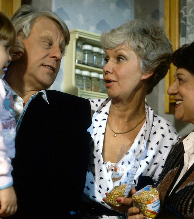 "Die Wicherts von nebenan: Der Prinz von Arkadien": Gerda (Inge Wolffberg) hat eine Tüte Mais für Popcorn in der Hand. Eberhard (Stefan Orlac) hat Kathrinchen (Sophie Birkner) auf dem Arm. Zusammen mit Hannelore (Maria Sebaldt) freuen sich alle über das Enkelkind.