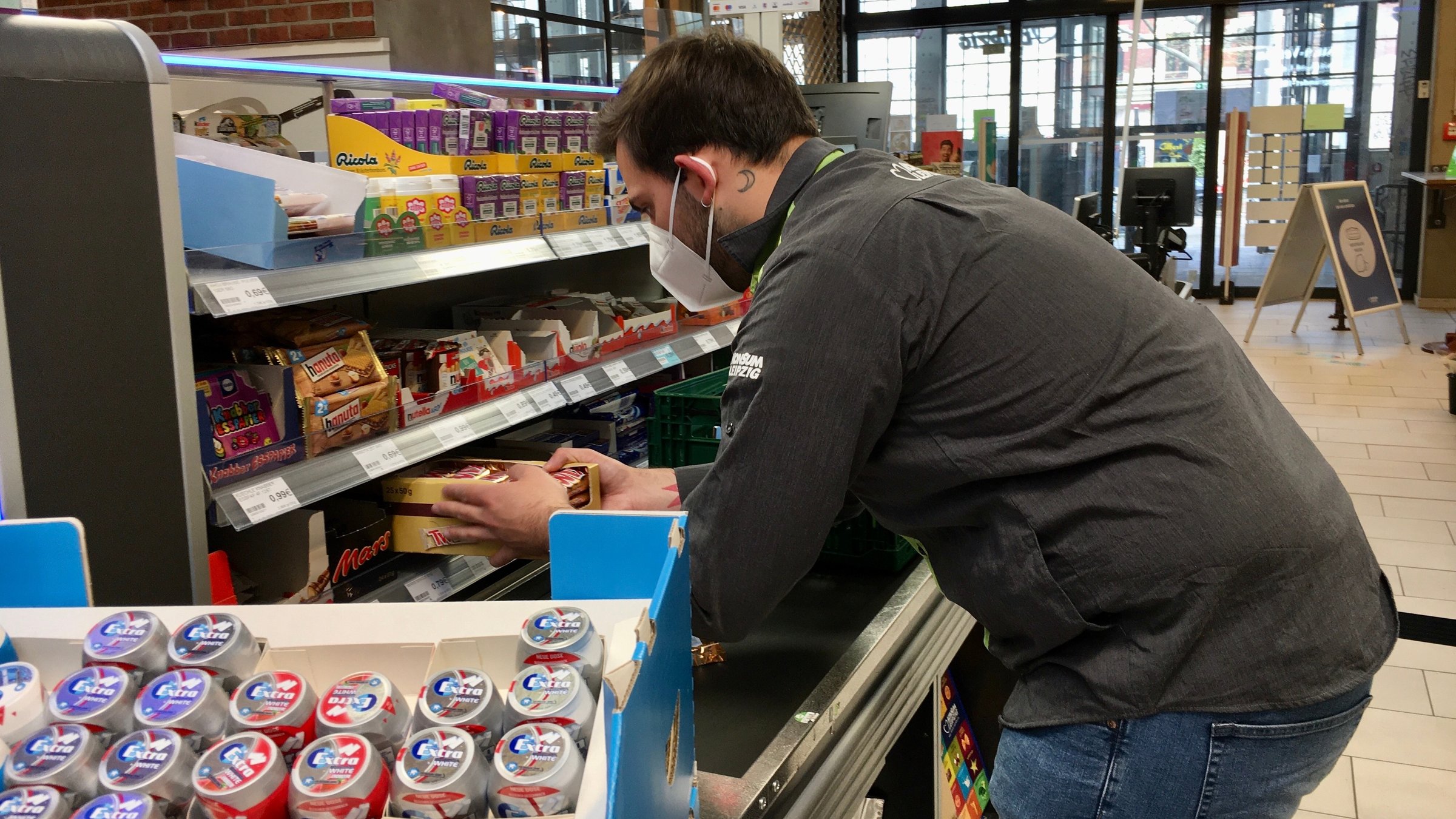 "37° Da kannst du einpacken - Verkäufer*innen im Einsatz": Supermarktangestellter steht vor einem Regal und räumt Ware ein.