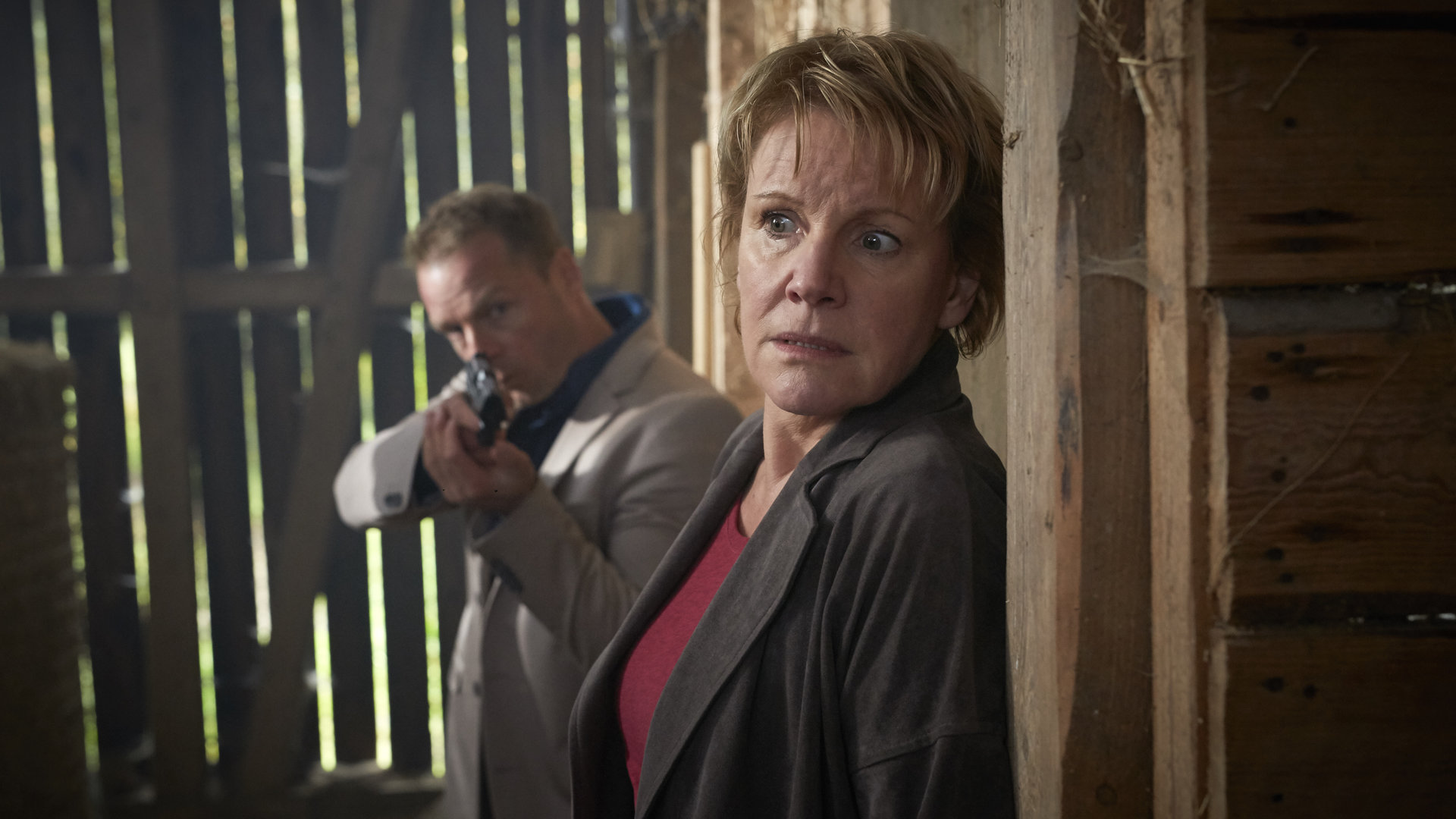 "Marie Brand und die Spur der Angst": Marie Brand (Mariele Millowitsch) steht ängstlich mit dem Rücken an einer Wand in einem Pferdestall. Simmel (Hinnerk Schönemann) kommt von hinten mit der Waffe im Anschlag an sie heran.