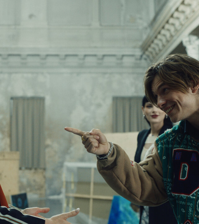 "Crystal Wall - Väter": Valerie (Barbara Meier) und Magdalena (Phenix Kühnert) stehen mit Nicolas Dardenne (Gustav Schmidt), der mit dem Finger in Valeries Richtung deutet, in einer großen Halle.