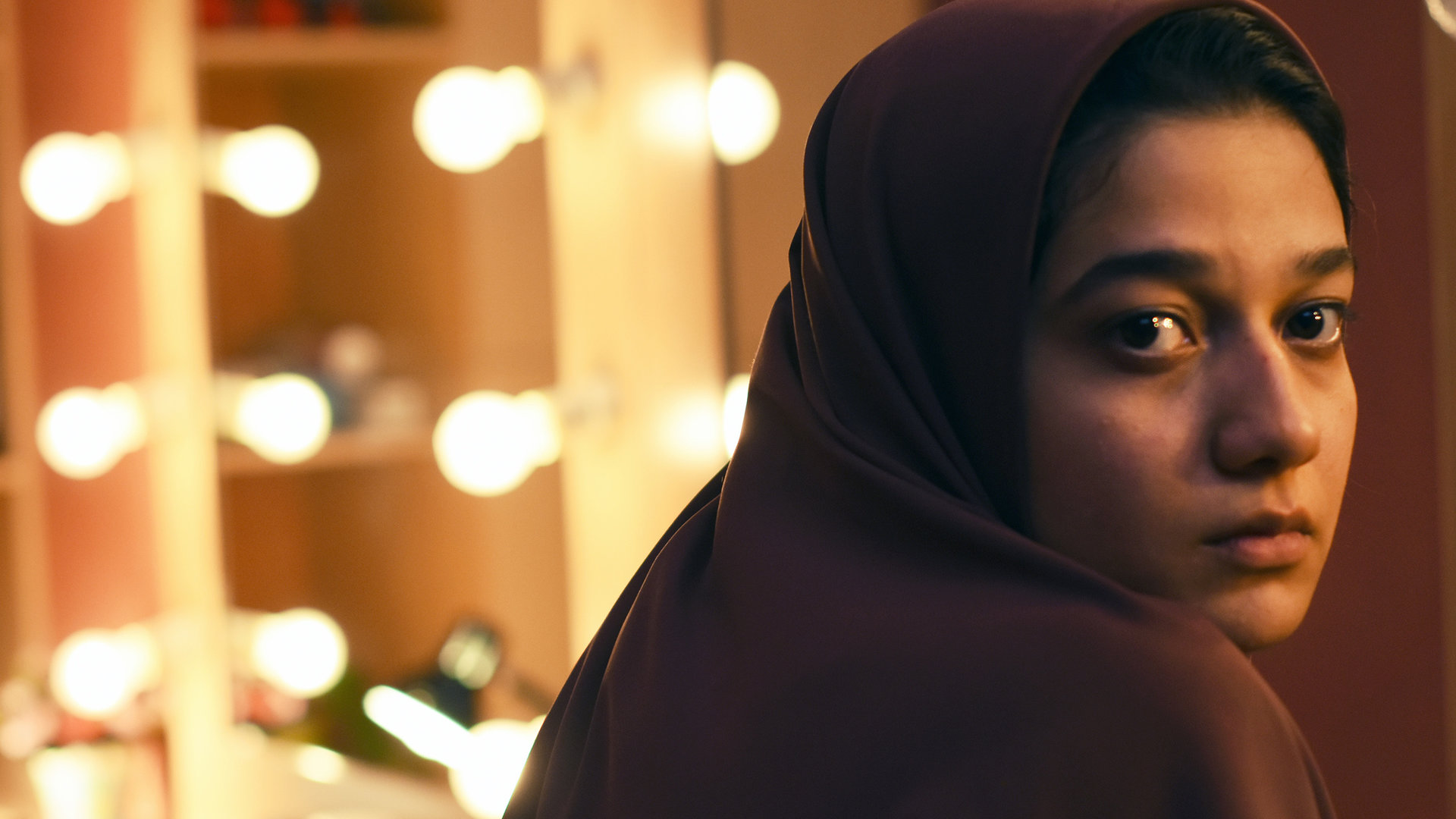 "Yalda": Maryam (Sadaf Asgari) sitzt von einem beleuchteten Schminkspiegel abgewandt. Sie trägt ein Kopftuch und blickt ängstlich über ihre rechte Schulter.