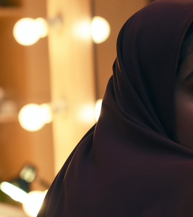 "Yalda": Maryam (Sadaf Asgari) sitzt von einem beleuchteten Schminkspiegel abgewandt. Sie trägt ein Kopftuch und blickt ängstlich über ihre rechte Schulter.